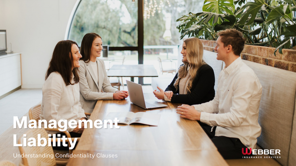 A group of four people, two women and two men, are sitting at a wooden table in a modern office environment. They are engaged in a discussion and smiling. A laptop is open on the table. Text on image reads: "Management Liability: Understanding Confidentiality Clauses for Better Workplace Trust.