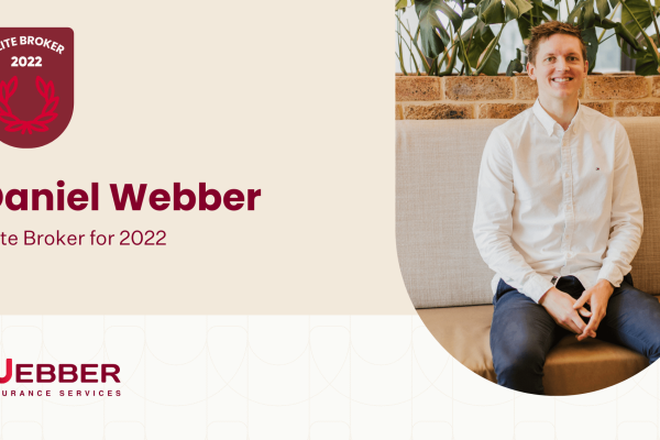 A man in a white shirt and dark pants is sitting on a beige couch, smiling. The text reads "Daniel Webber, Elite Broker for 2022" next to a badge that says "Daniel Webber Elite Broker 2022" above the logo "Webber Insurance Services." The background is beige with plants visible.
